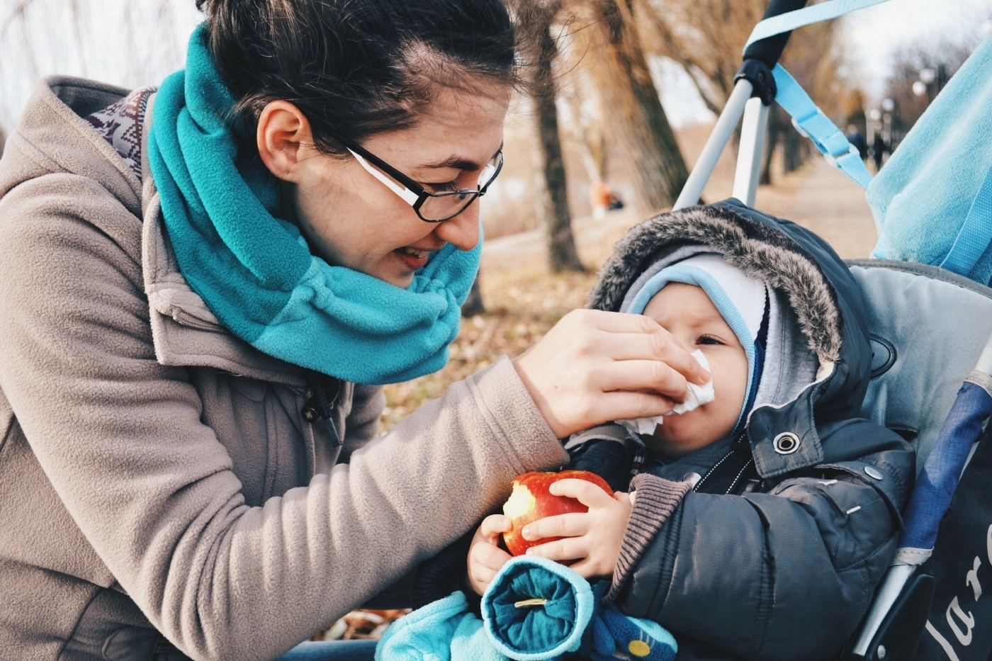 Mother wiping her toddler's nose as they sit bundled in a stroller