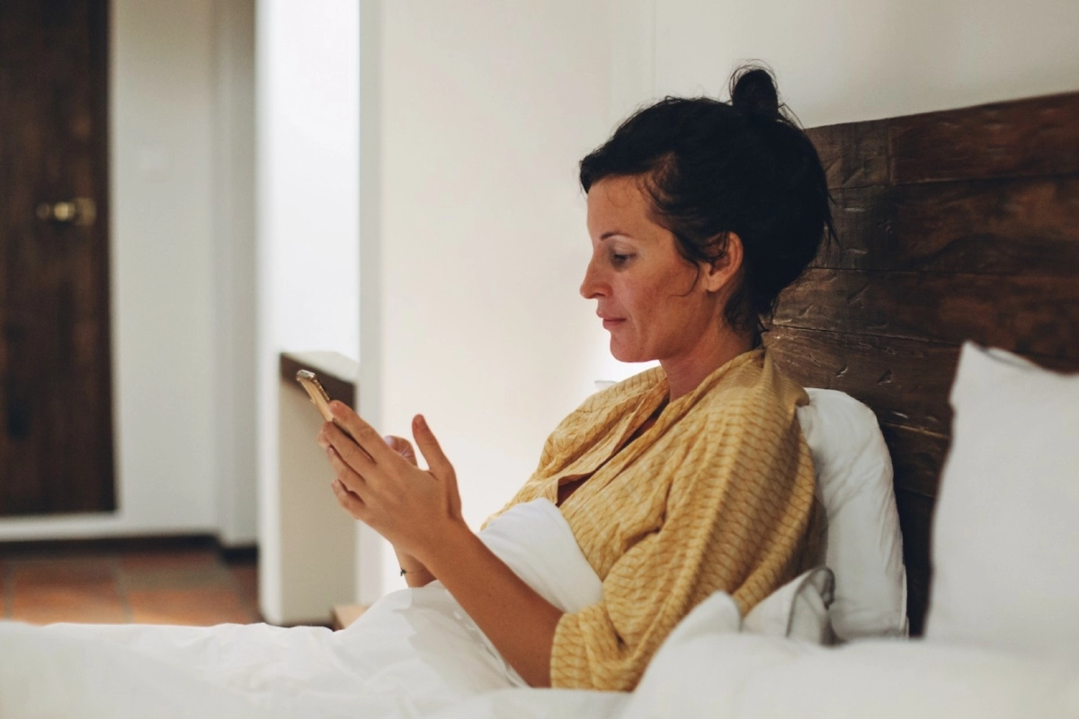 Woman sitting up in bed looking at her phone