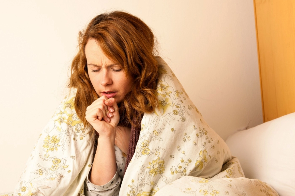 Woman with a comforter over her shoulders coughing.