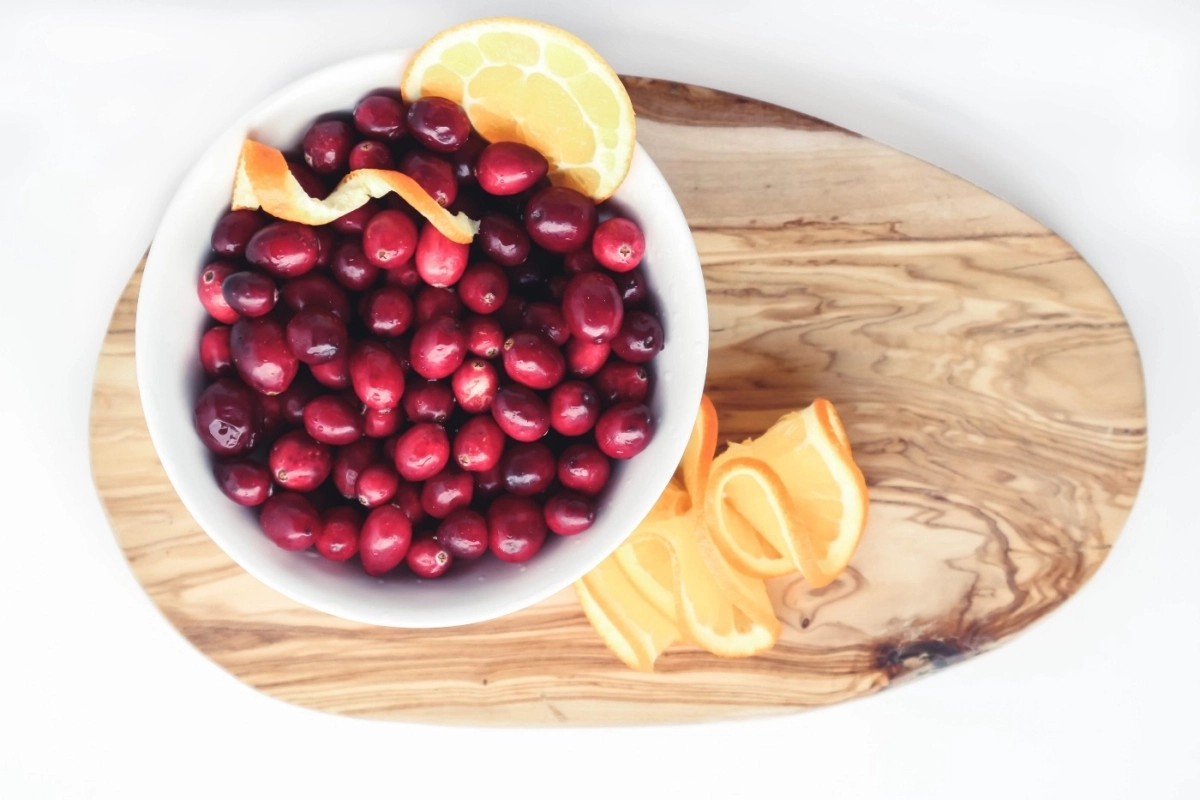A bowl of cranberries with citrus, sitting on a cutting board