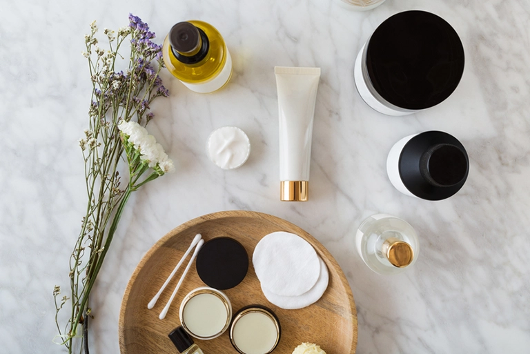Various beauty products sitting on a marble countertop next to flowers