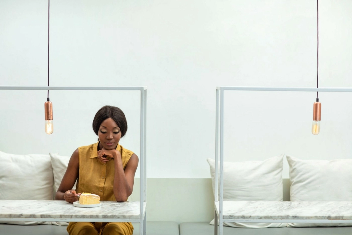Woman sitting at a stark table looking at a piece of cake