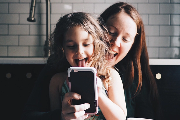 A woman and her young daughter smiling and looking at a smartphone