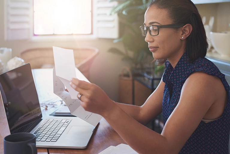 A woman sitting at a desk, looking at papers and her laptop