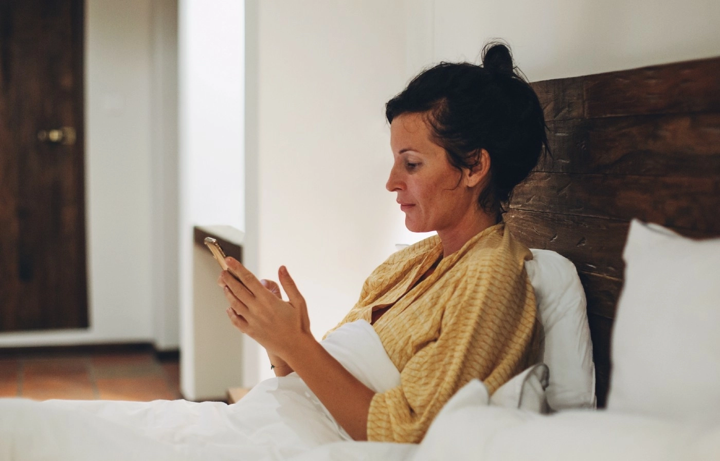Woman sitting up in bed looking at her phone