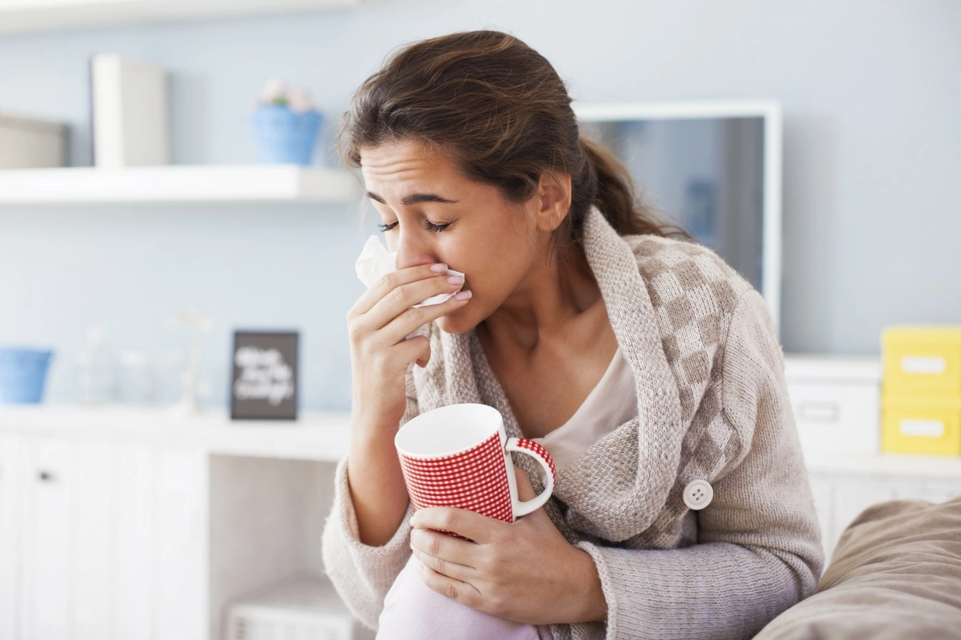 A woman sneezing into a tissue and holding a mug
