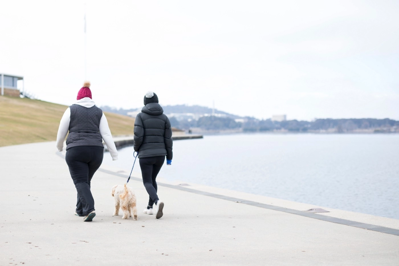 Two people walking their dog by a body of water