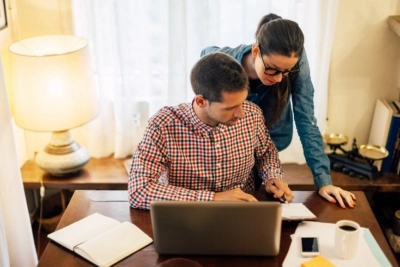 A woman and man leaned over a desk looking at paperwork and a laptop