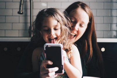 A woman and her young daughter smiling and looking at a smartphone