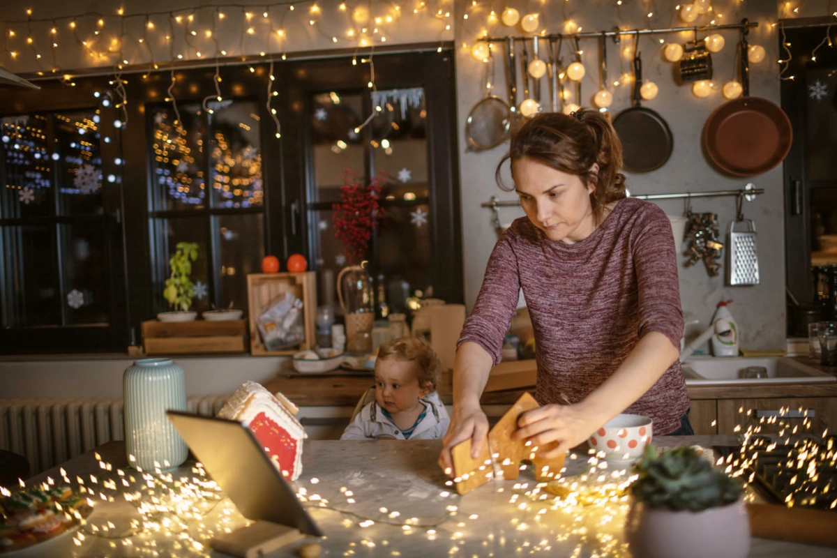 Mother making homemade gingerbread house on a Christmas Eve for her family. She looks up a digital tablet recipe for it.