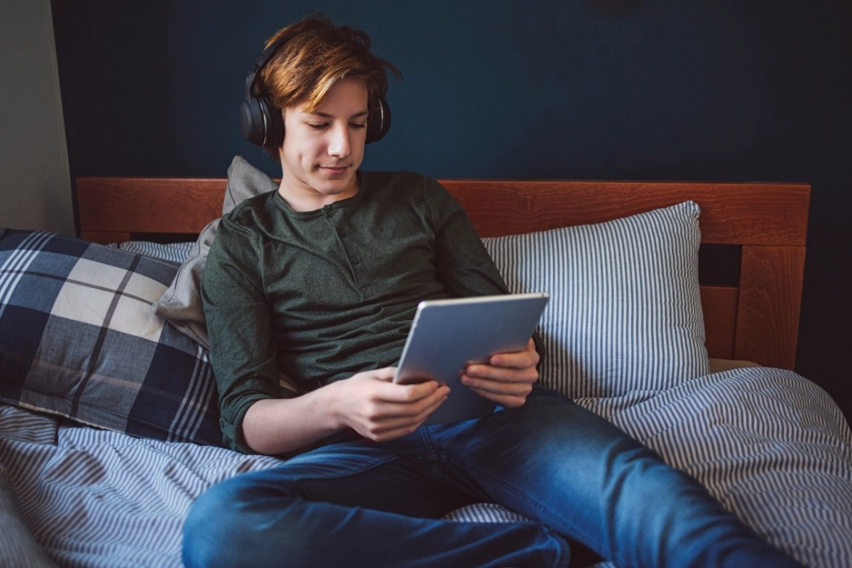 teenager on bed with looking at ipad wearing headphones