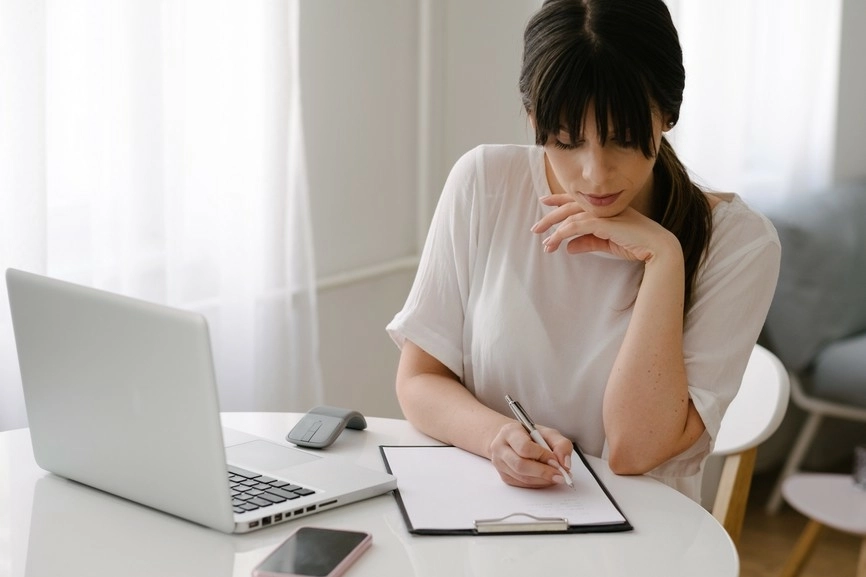 woman sitting at computer writing on paper