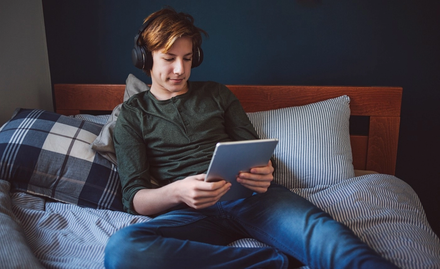 teenager on bed with looking at ipad wearing headphones