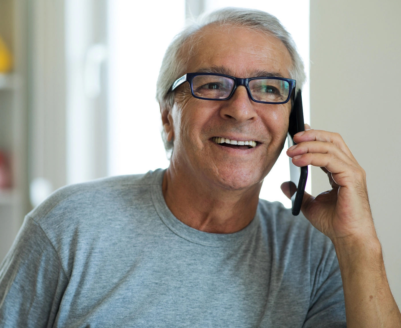 man with gray hair and black glasses talking on his phone