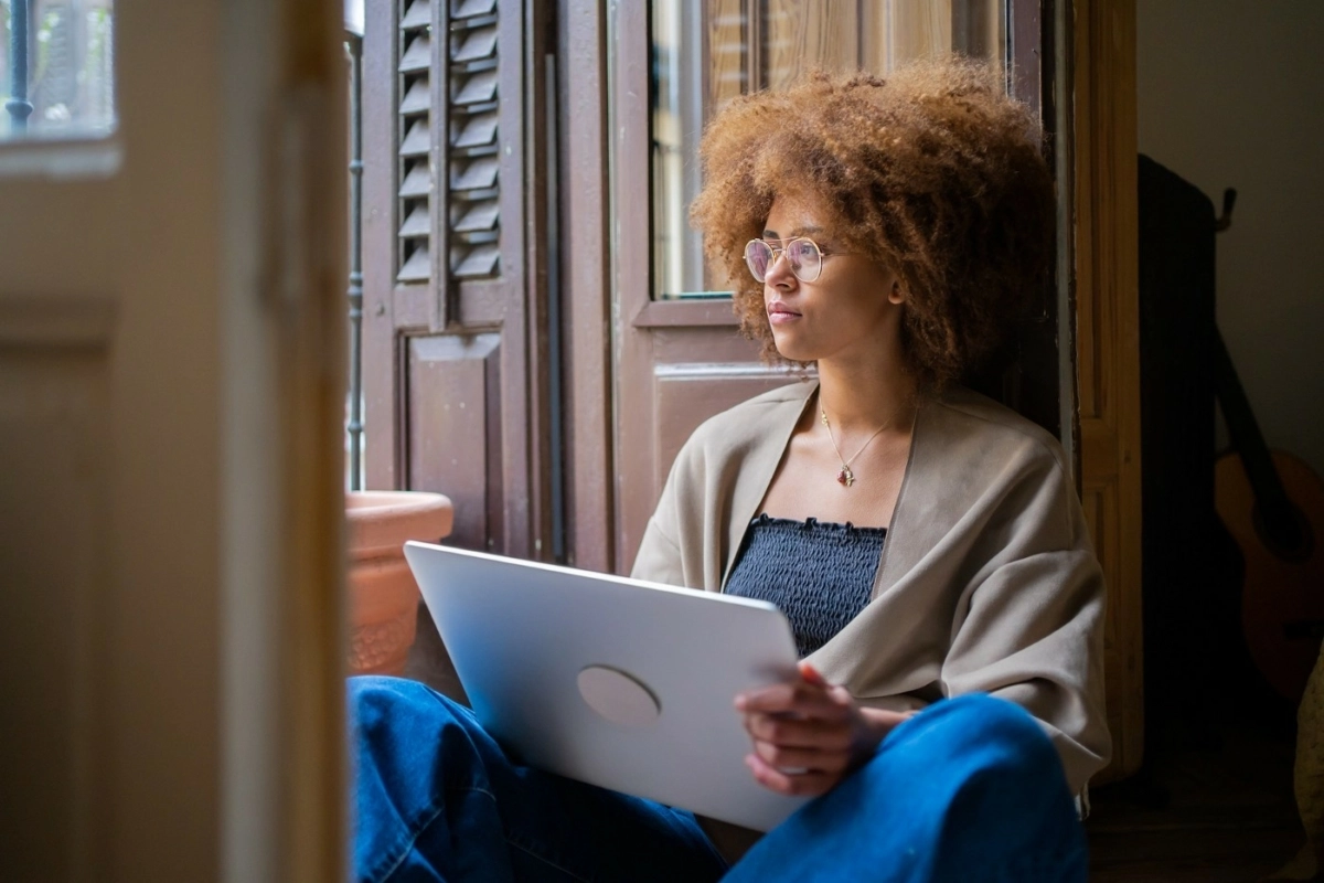 young woman staring outside holding her laptop.