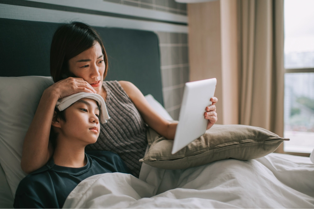 mom and son in bed using ipad for sick telehealth visit.
