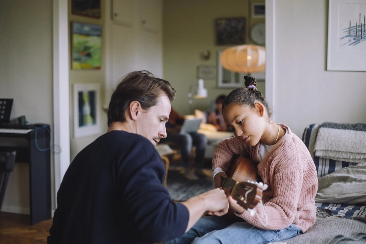 Dad helping daughter learn to play guitar.
