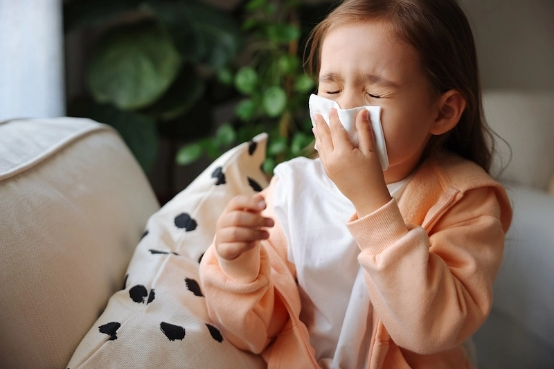 young girl sneezing into a tissue