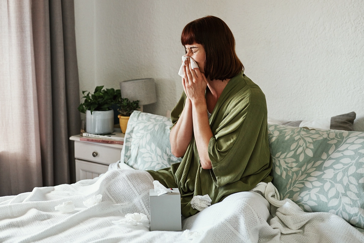 A woman blowing her nose while in bed.