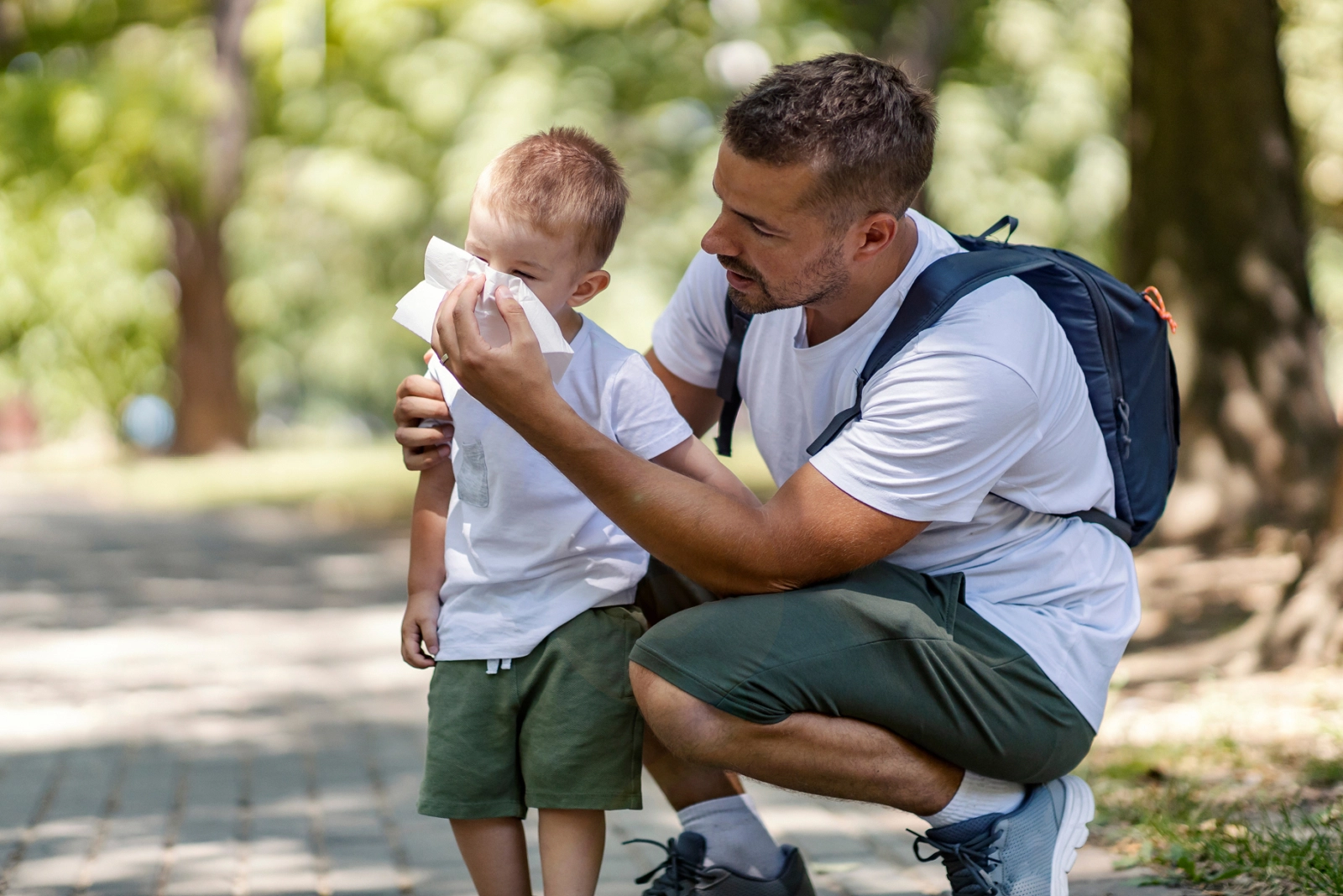 A father holding a tissue for his son outside in a park.