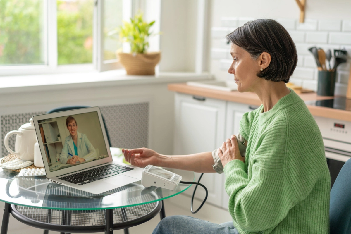 An older woman sitting at a desk and taking her blood pressure.